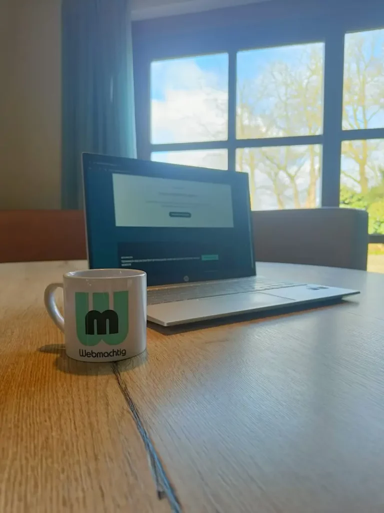 Laptop met een Webmachtig-mok bij het raam